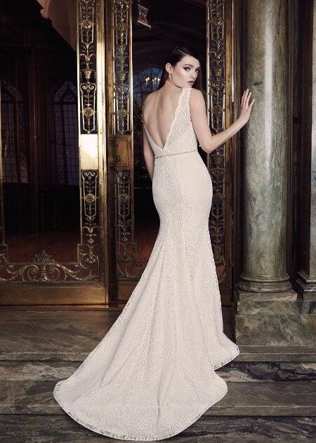 Woman in a backless ivory gown standing in a doorway of an ornate room, looking over her shoulder