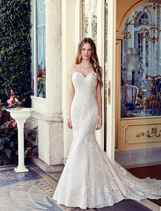 Woman in a white lace wedding gown standing at a doorway beside an ornate building facade