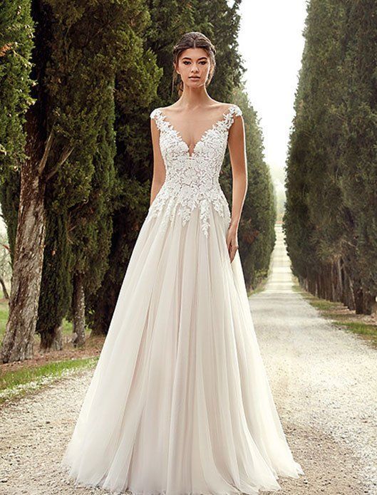 Woman in a white lace gown standing on a tree-lined path outdoors