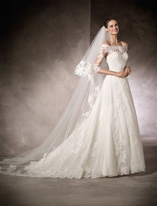 Bridal gown with long lace train and veil displayed against a studio backdrop