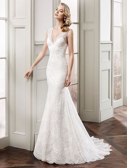Woman in a white lace wedding dress standing in a bright room by open doors