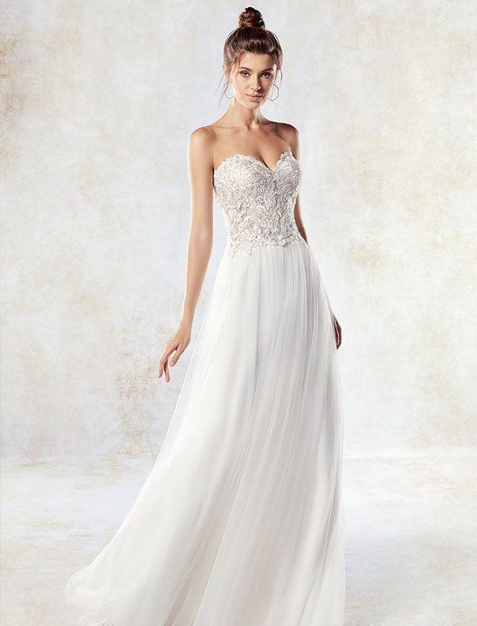 Woman in a white beaded strapless gown with flowing skirt, standing against a light studio backdrop