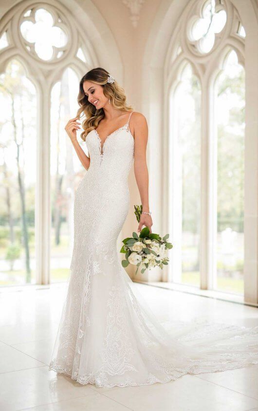 Bride in a lace wedding gown holding a bouquet in a bright arched windowed room