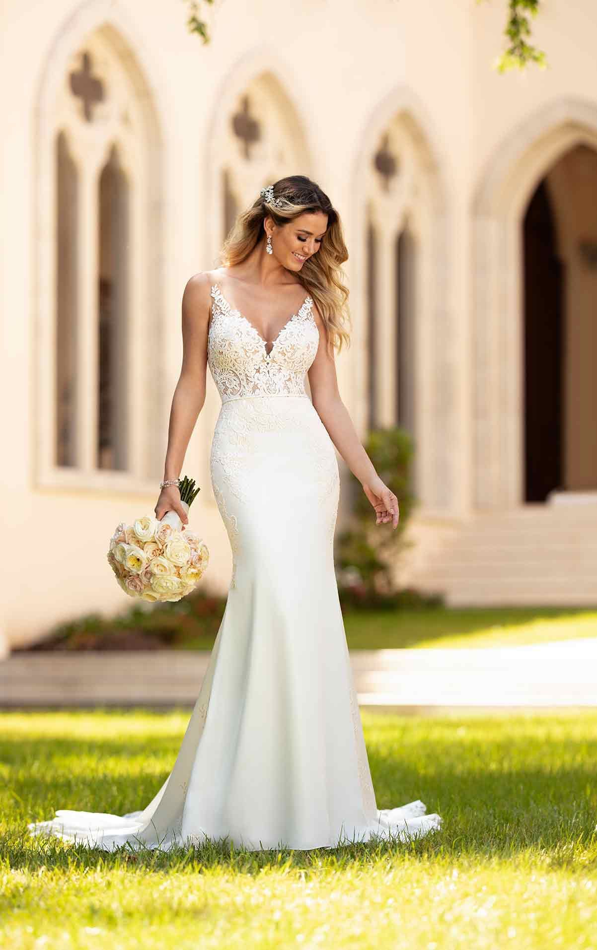 Bride in a white wedding dress walking on grass outside a chapel, holding a bouquet
