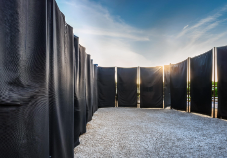 A row of black curtains are covering a gravel path.