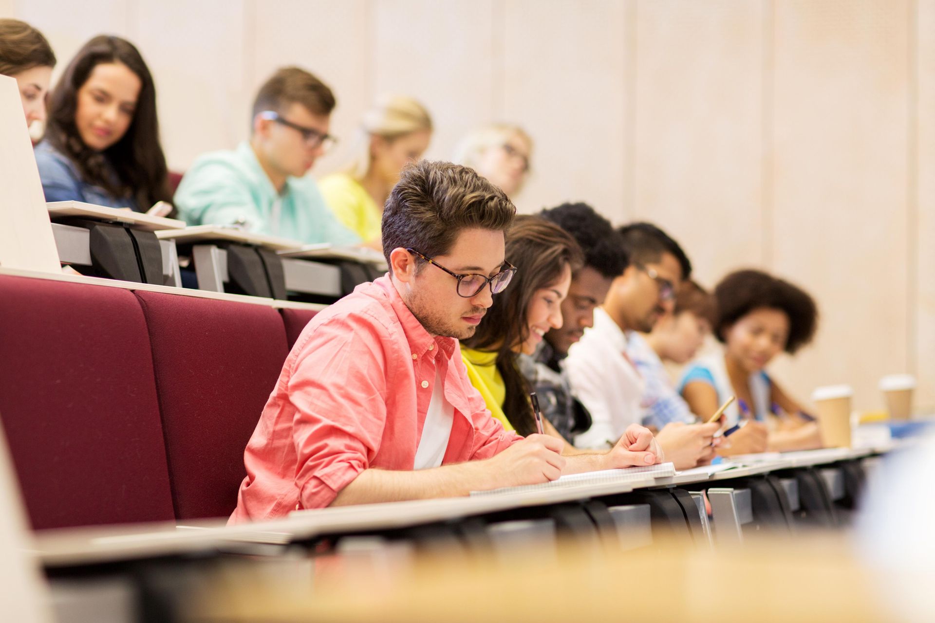 Students writing in notebooks in a tiered lecture hall.