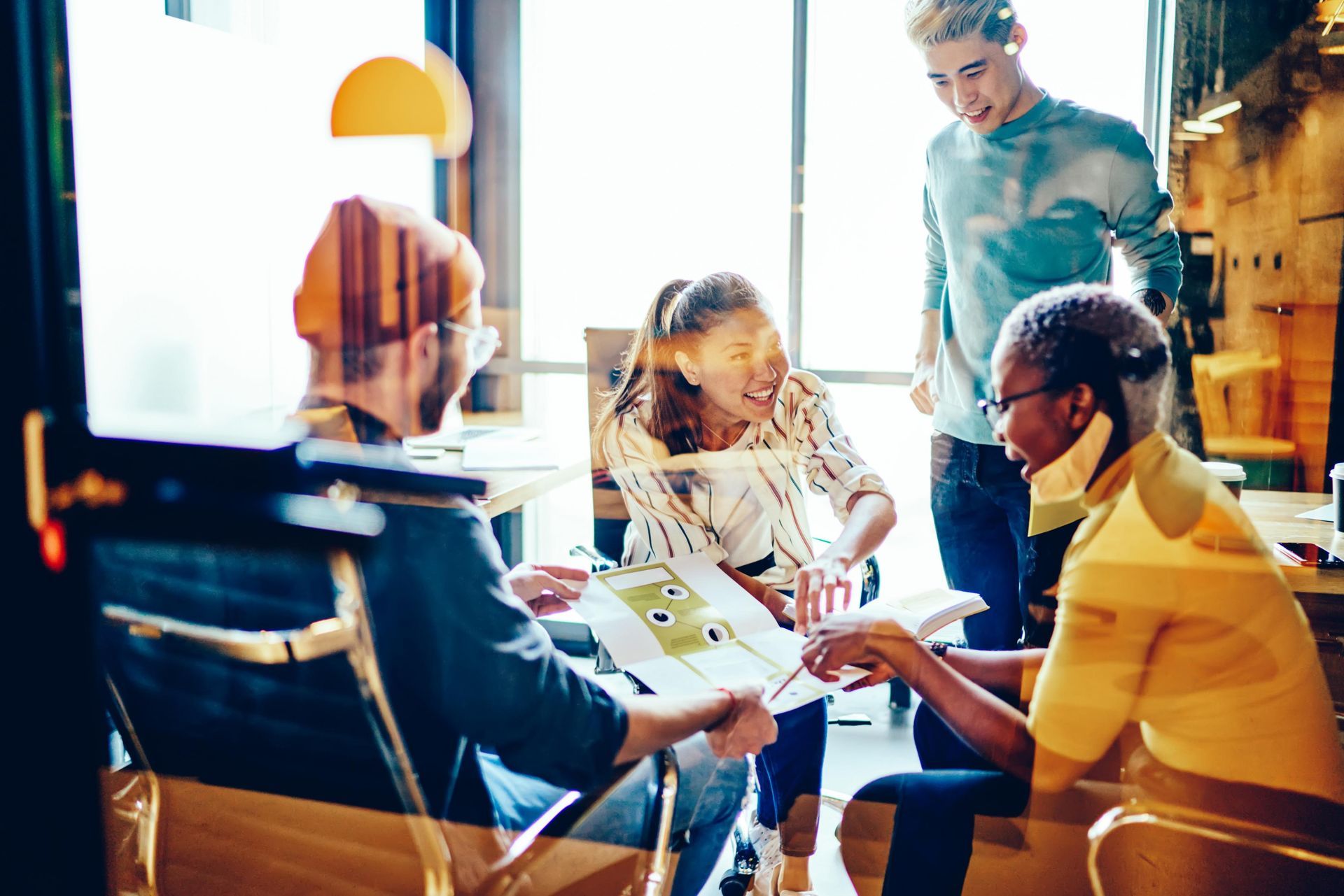 People in office reviewing papers; window light.