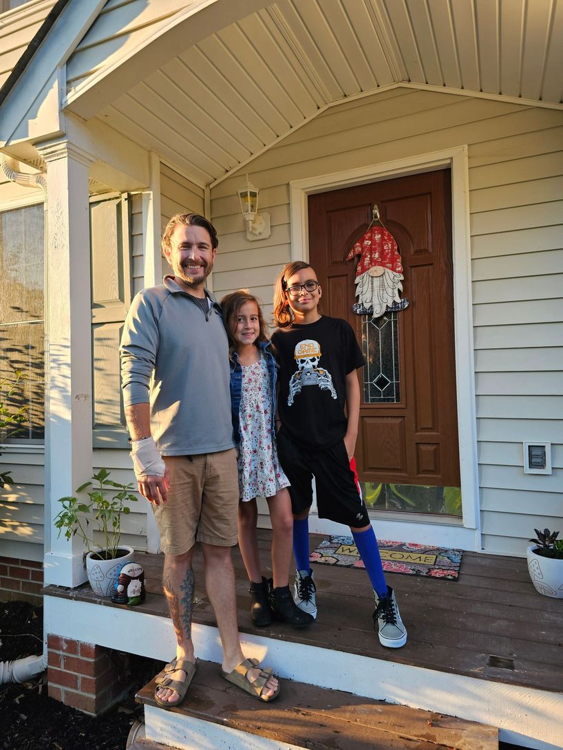 A man and two children are standing on the porch of a house.