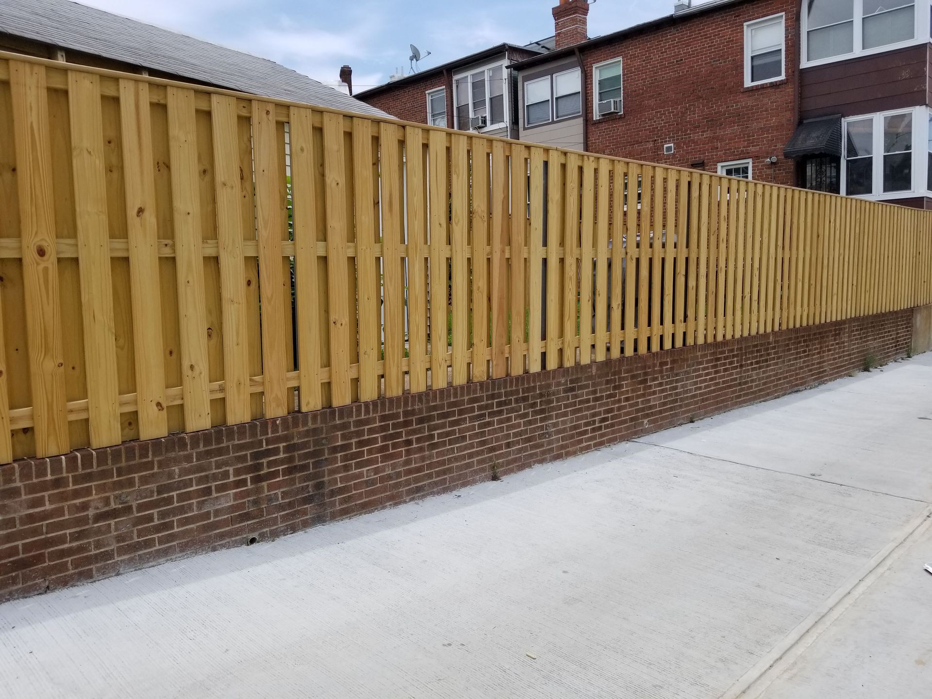 A wooden fence surrounds a brick wall in front of a house.