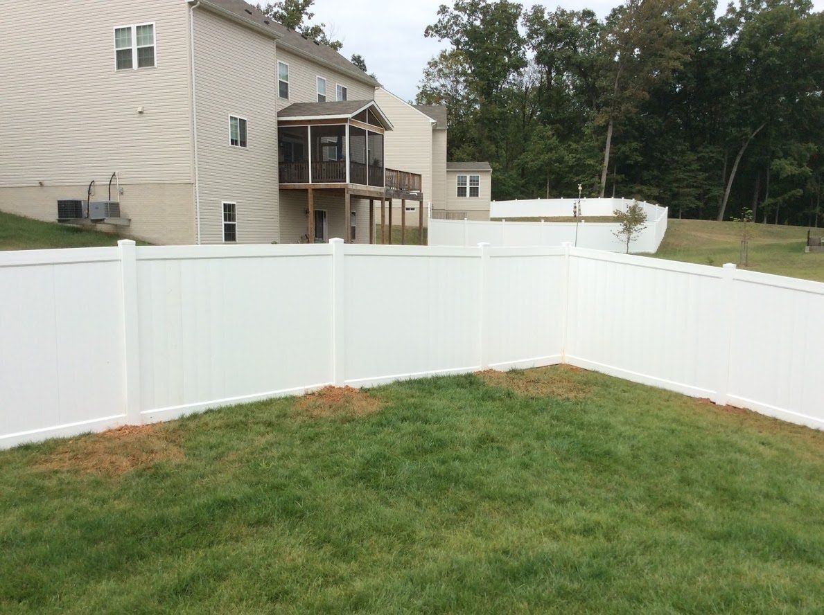 A white fence surrounds a lush green yard in front of a house.