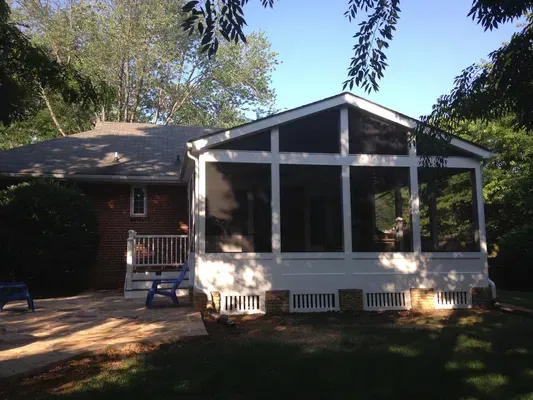 A screened in porch with a brick house in the background