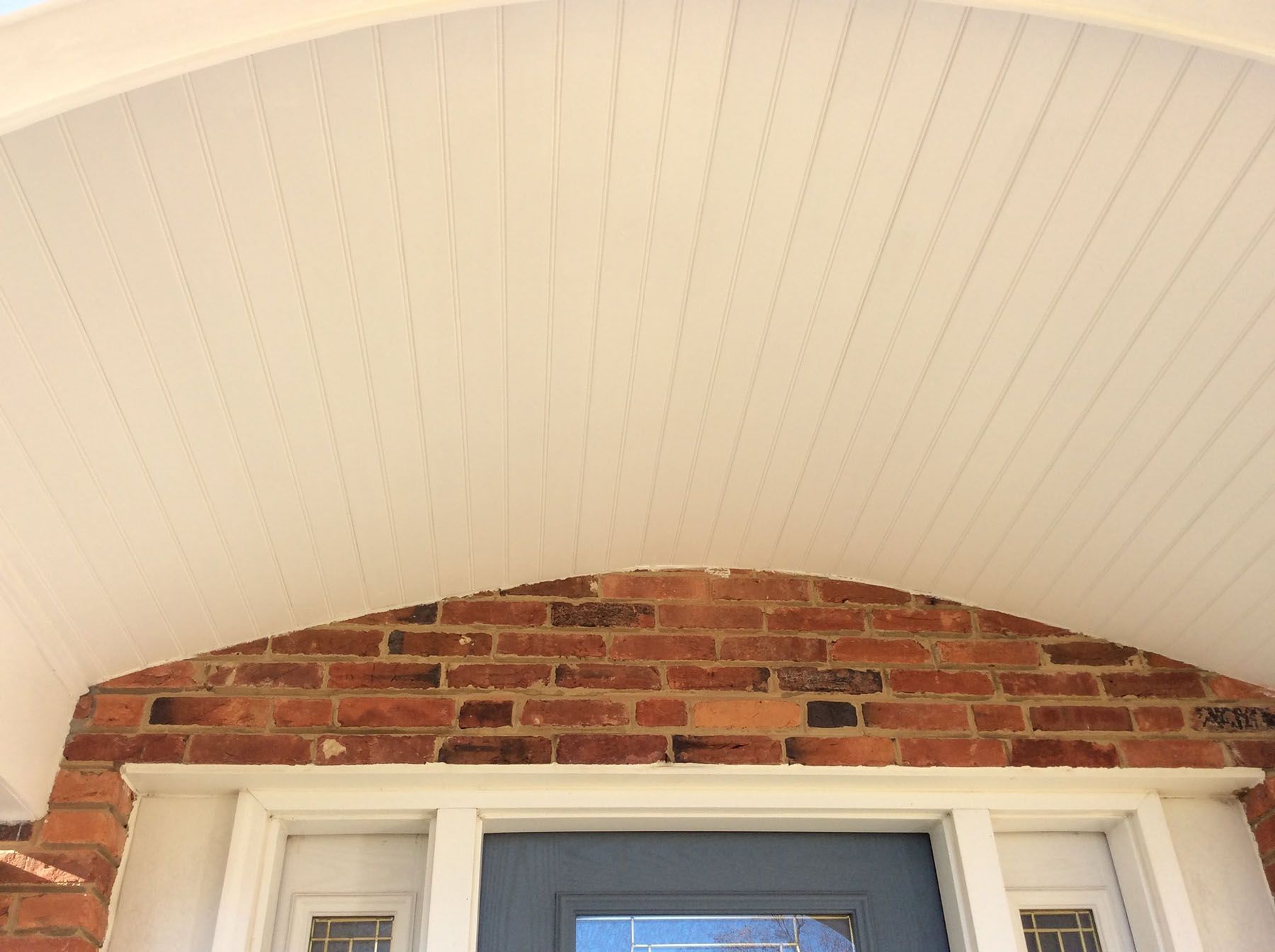 The ceiling of a porch with a brick wall and a blue door.