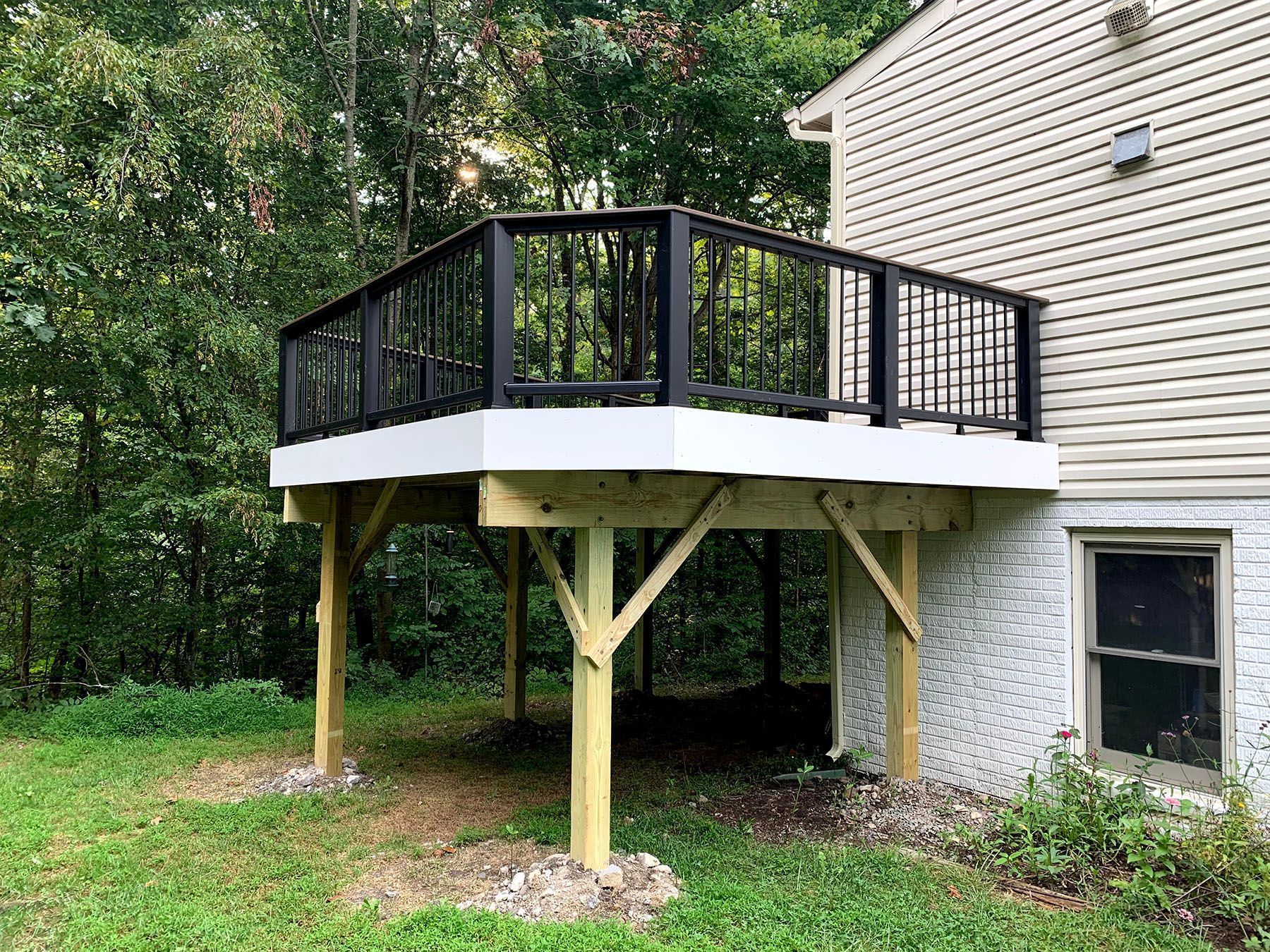 A wooden deck with a black railing is in the backyard of a house.