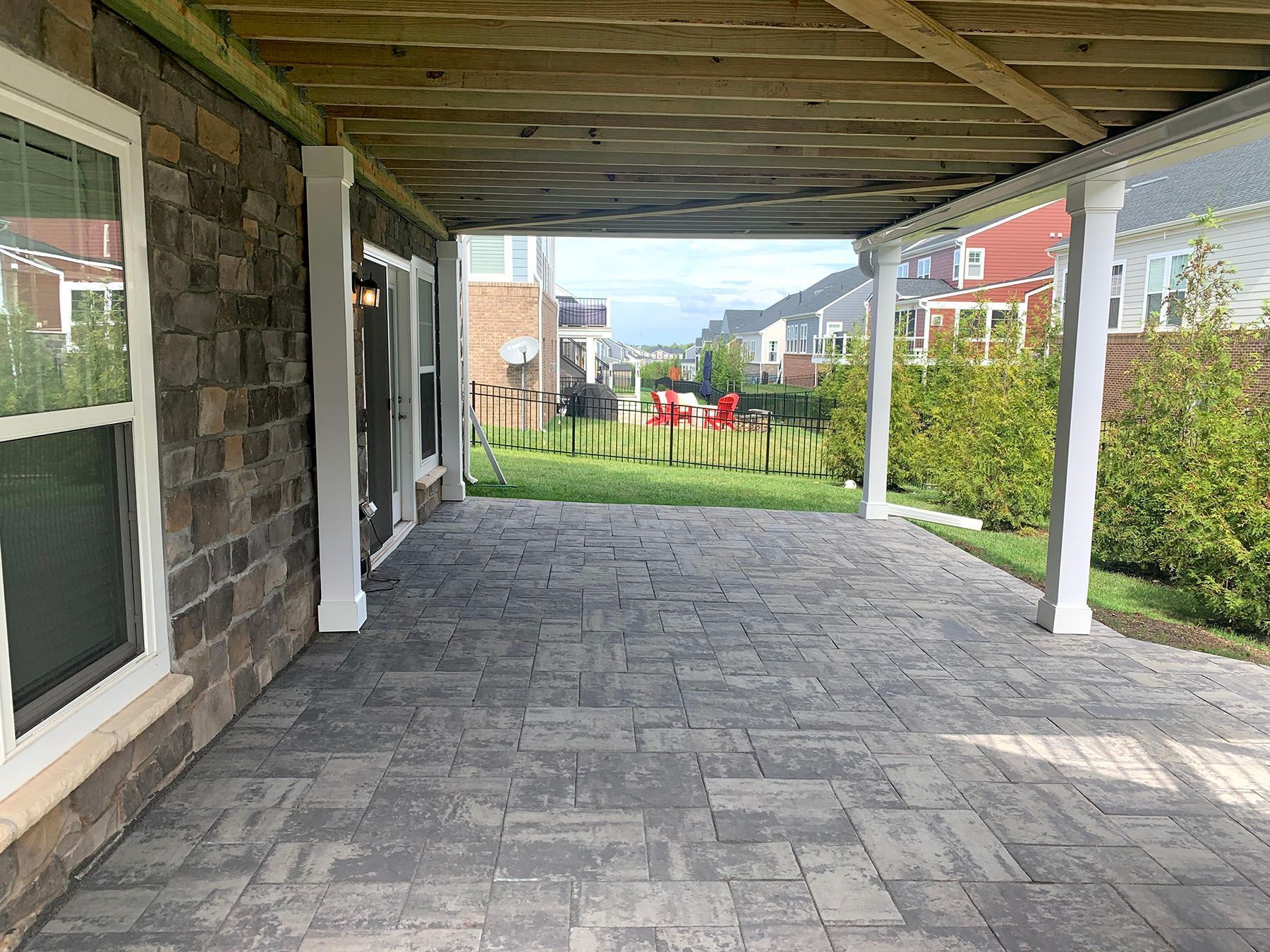 A covered patio with a view of a backyard and a house in the background.