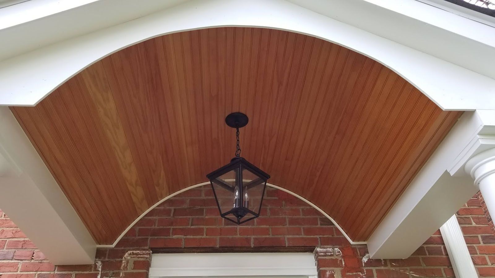 A porch with a wooden ceiling and a lantern hanging from it