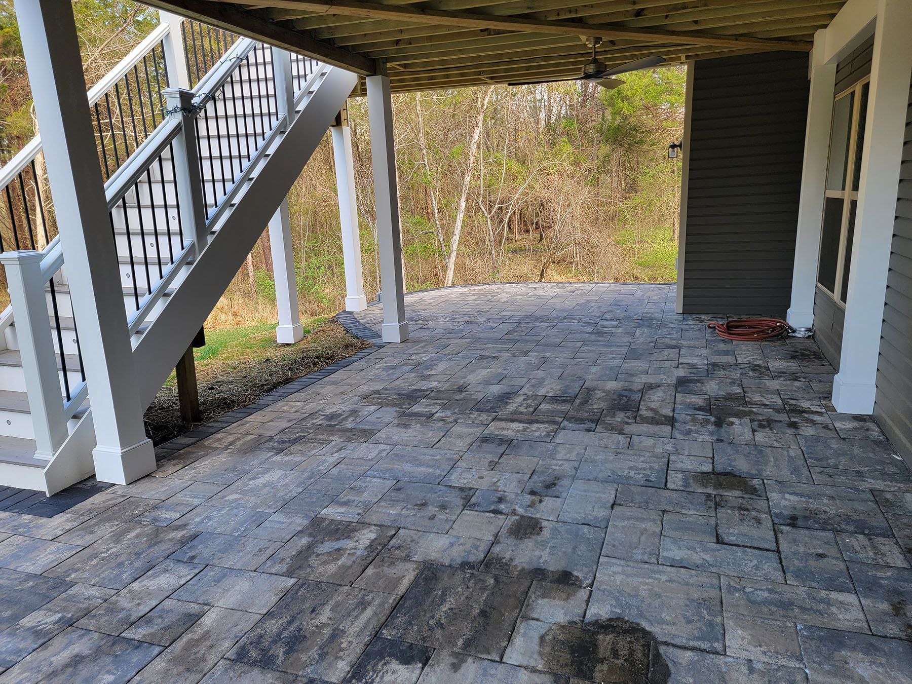 A patio under a deck with stairs leading up to it.