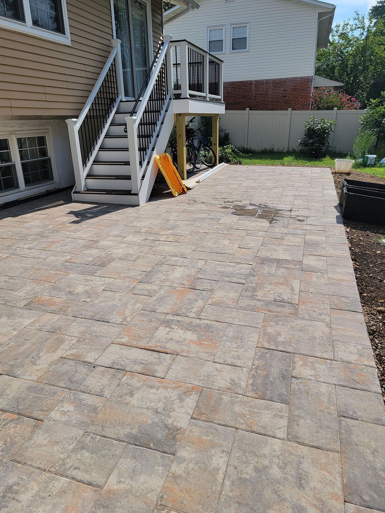 A patio with stairs leading up to a deck and a house in the background.