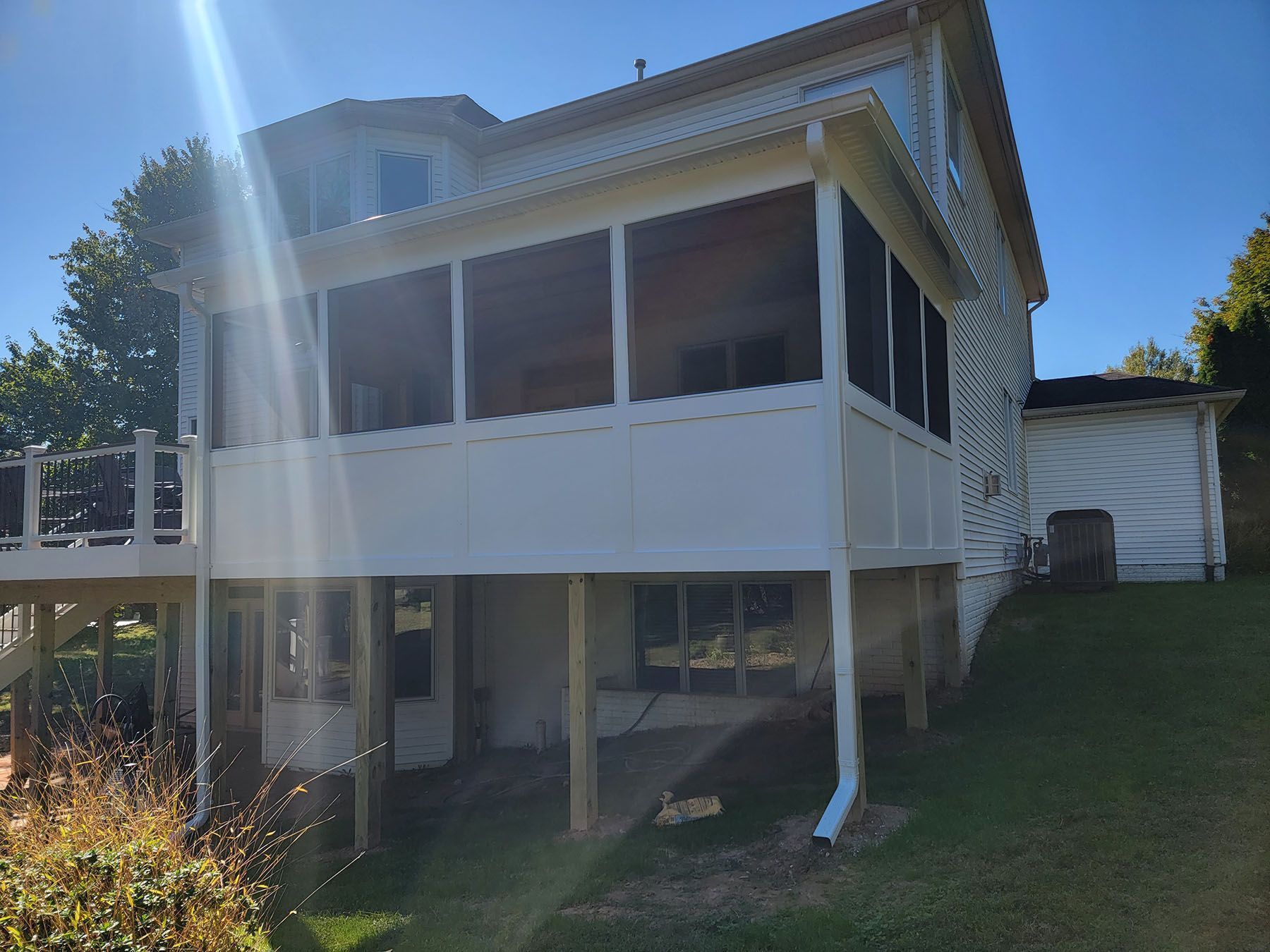 A white house with a screened in porch and a deck.