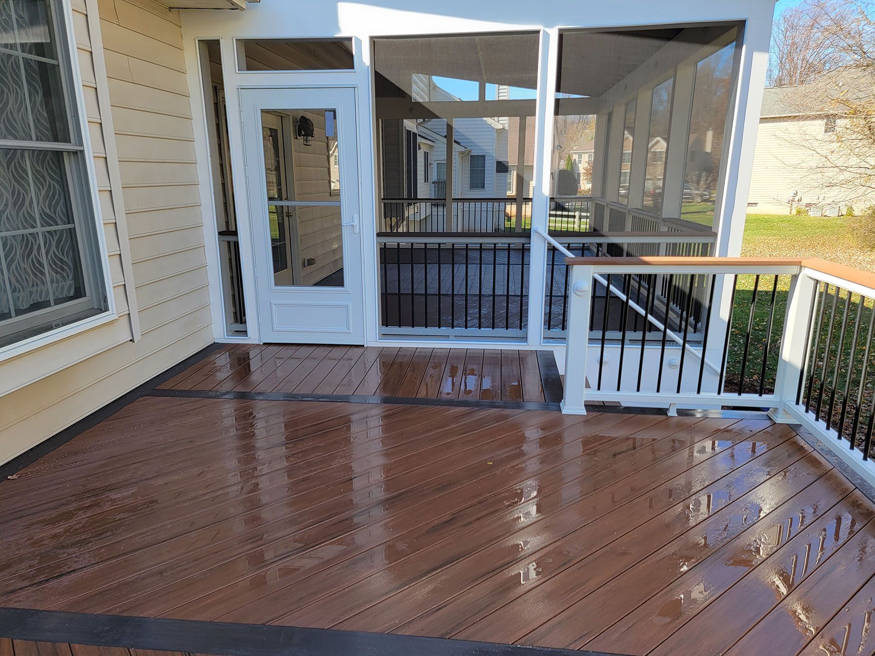 A screened in porch with a wooden deck and a white railing.