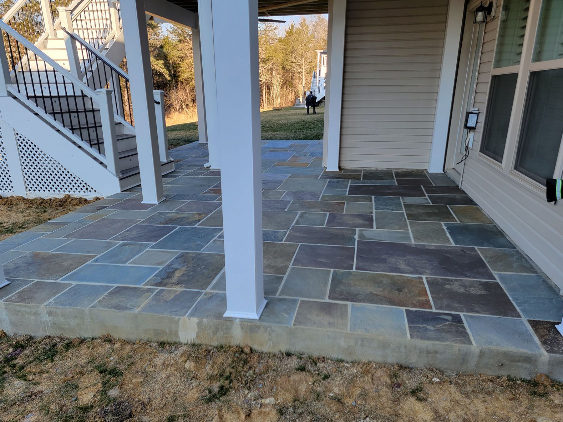 A patio with a staircase leading up to it and a white house in the background.
