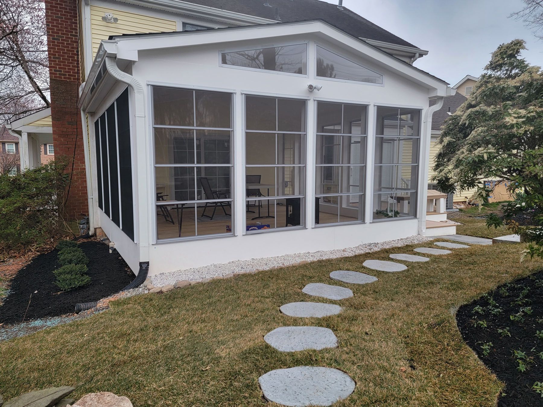 A screened in porch with a walkway leading to it is in the backyard of a house.
