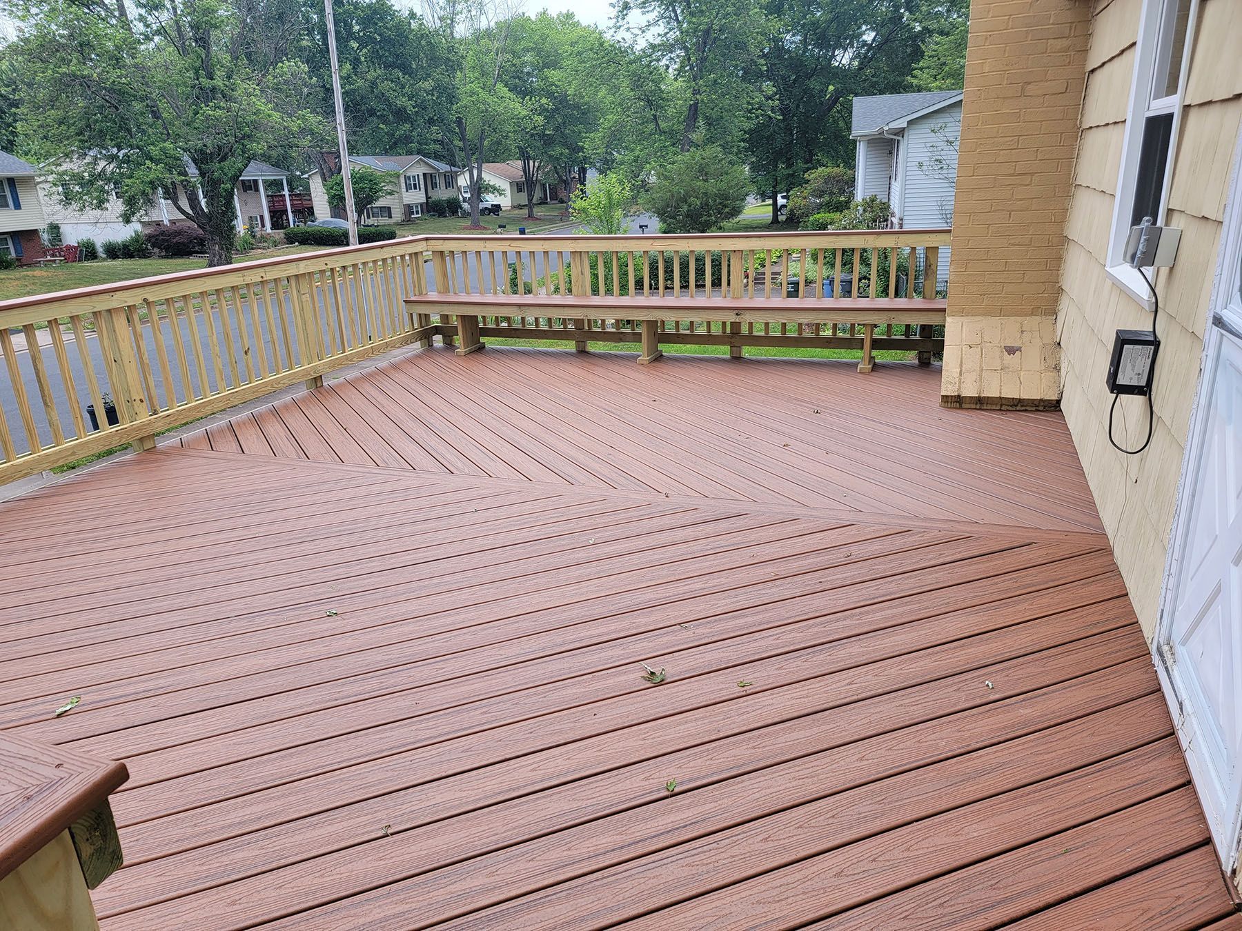 A large wooden deck with a wooden railing on the side of a house.