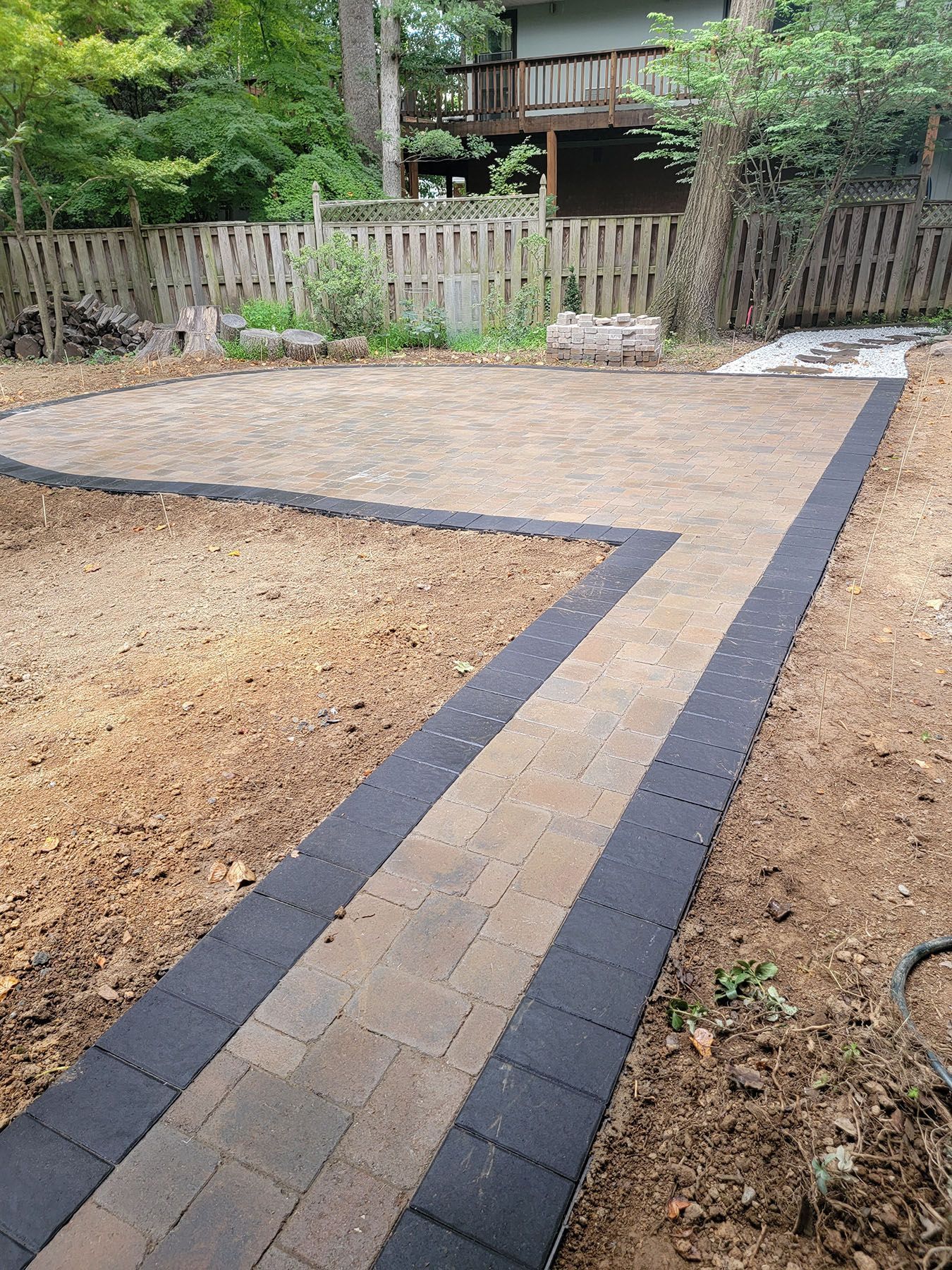 A brick walkway leading to a house with a fence in the background.