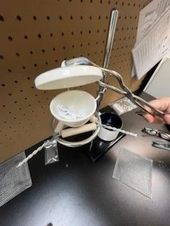 A person is holding a pair of tweezers over a stack of cups on a table.
