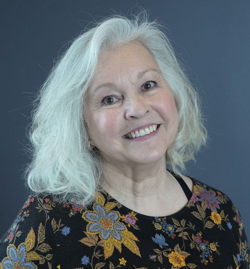 A woman with gray hair is smiling and wearing a floral shirt.