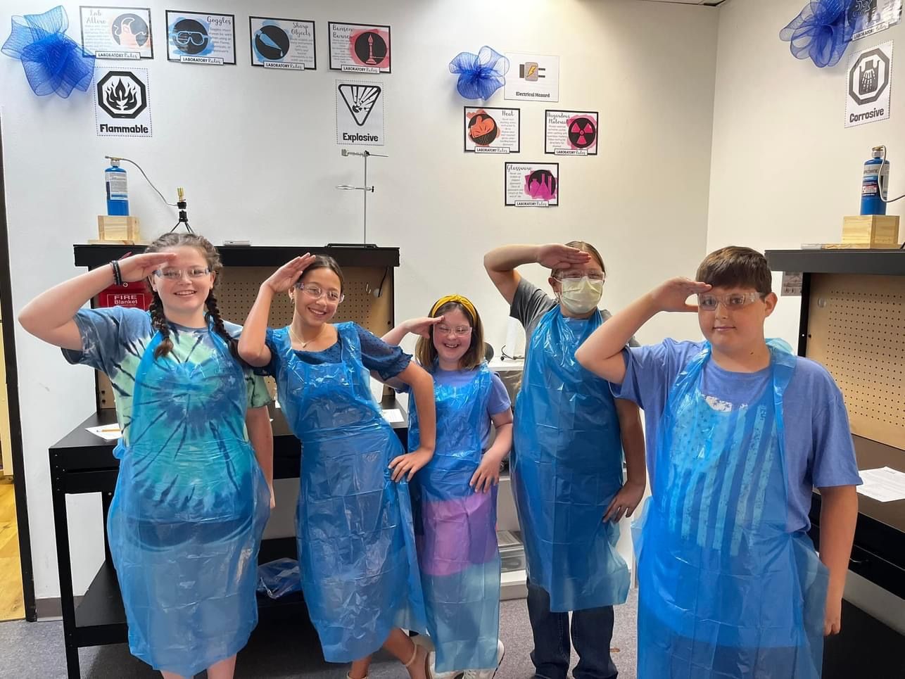 A group of children wearing blue plastic aprons are posing for a picture.