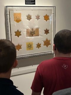 Two men are looking at a display of star badges on a wall.