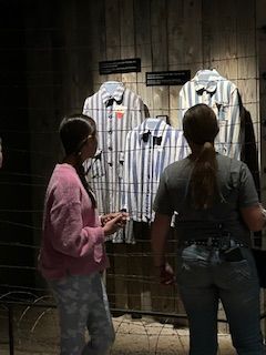 Two women are standing in front of a wall with shirts hanging on it.