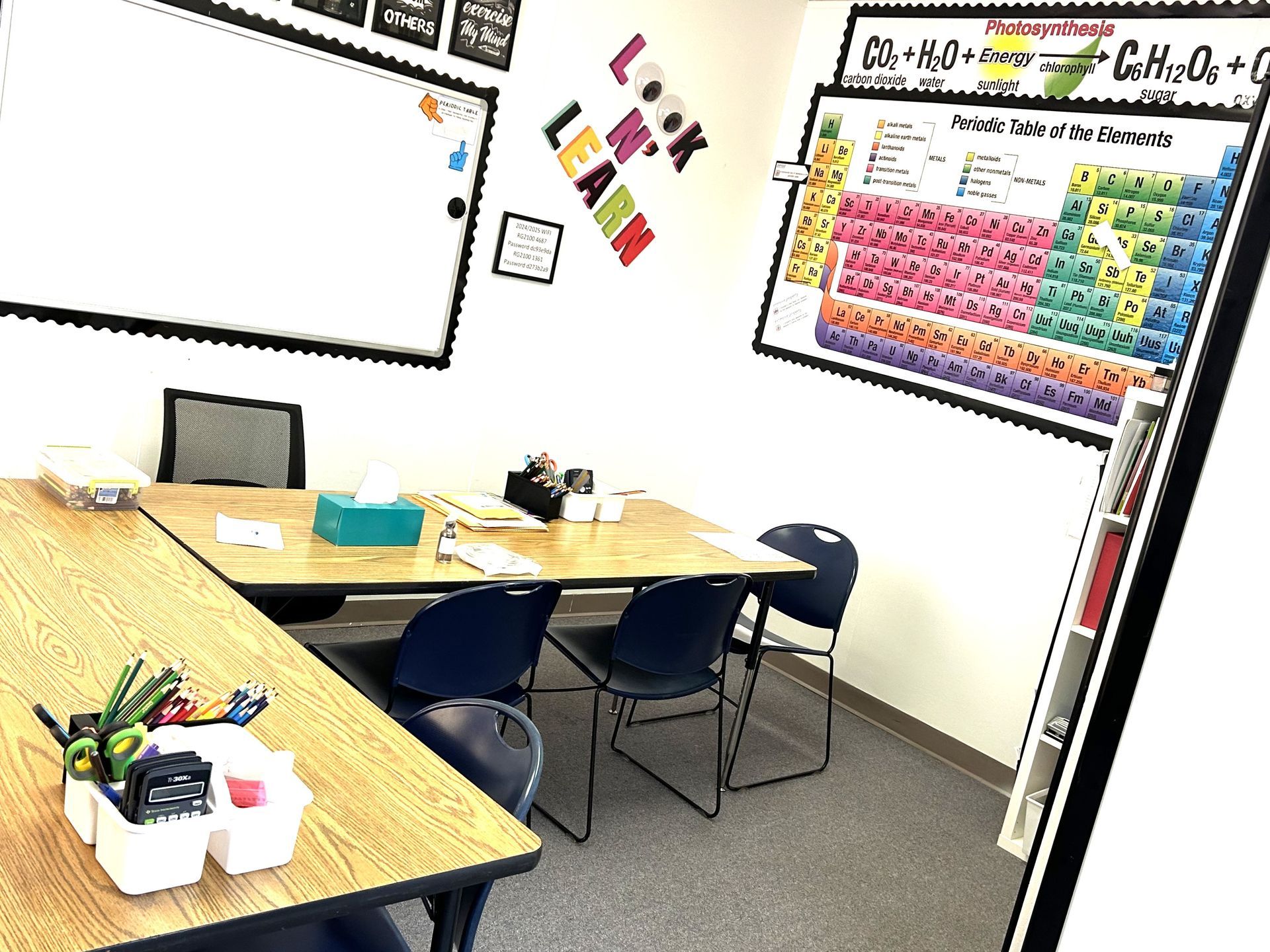 A classroom with tables and chairs and a periodic table on the wall.