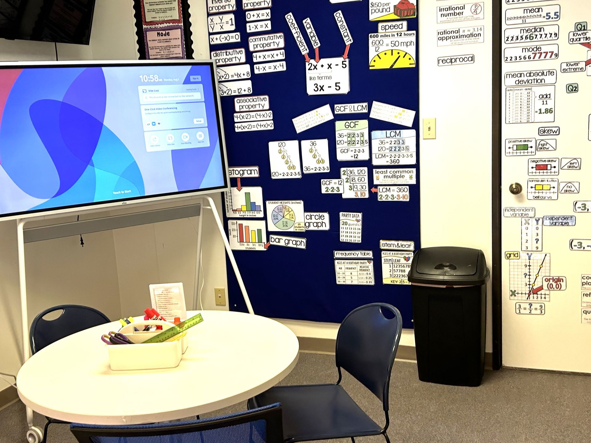 A classroom with a table and chairs and a large screen