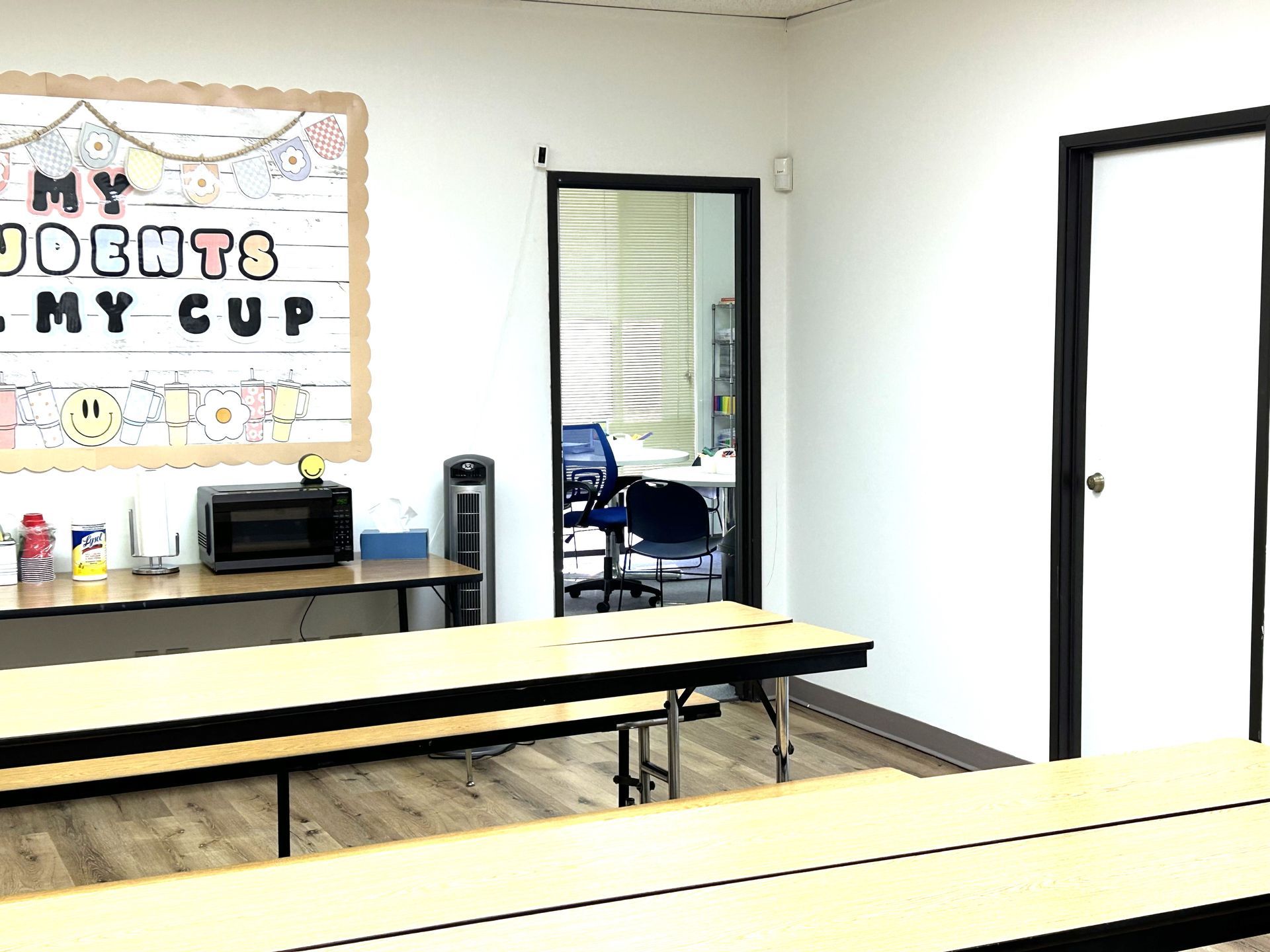 A classroom with tables and a sign on the wall that says `` my students my cup ''.