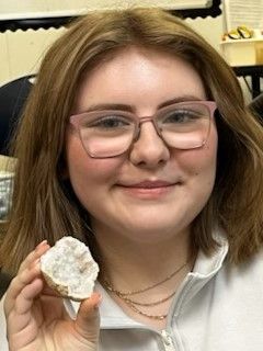 A young woman wearing glasses is holding a piece of rock in her hand.