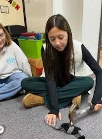 A girl is sitting on the floor holding a hammer and a pair of socks.