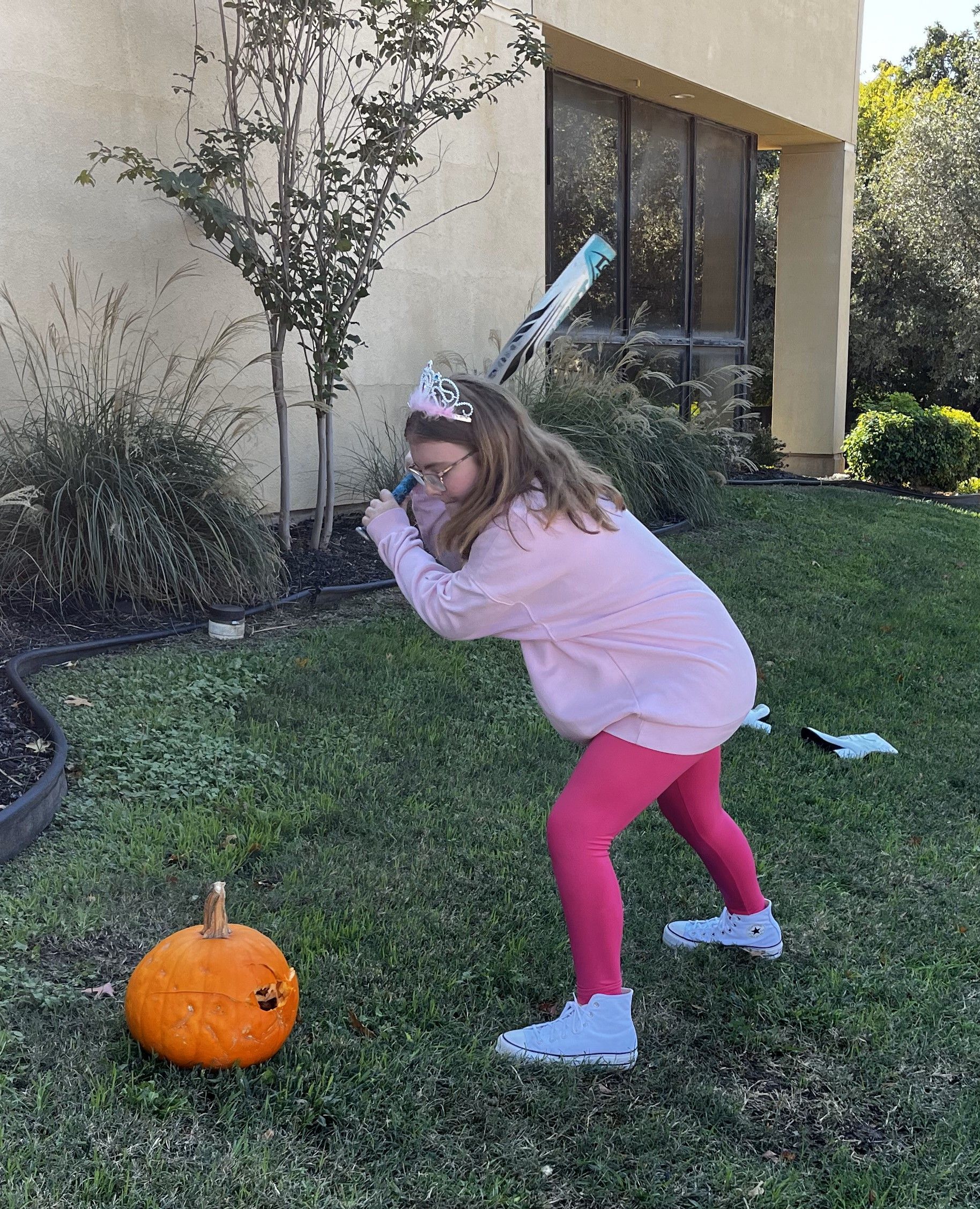 A little girl is holding a baseball bat in front of a pumpkin.