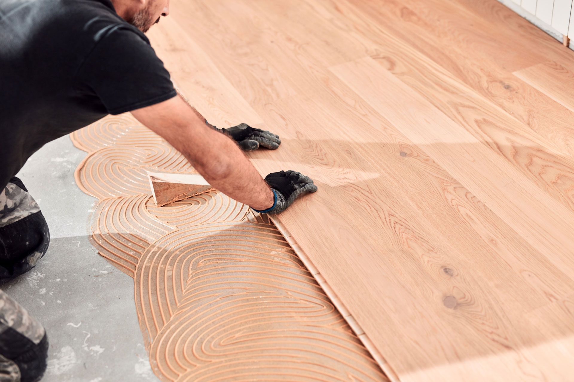 Man installing wood flooring, applying glue with a notched trowel.