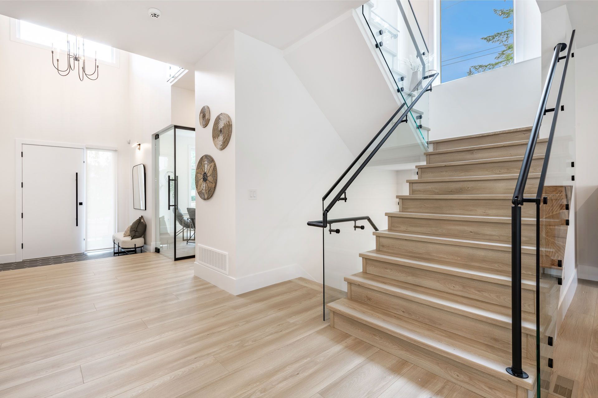Bright entryway with light wood floors, staircase, glass railing, and modern decor.