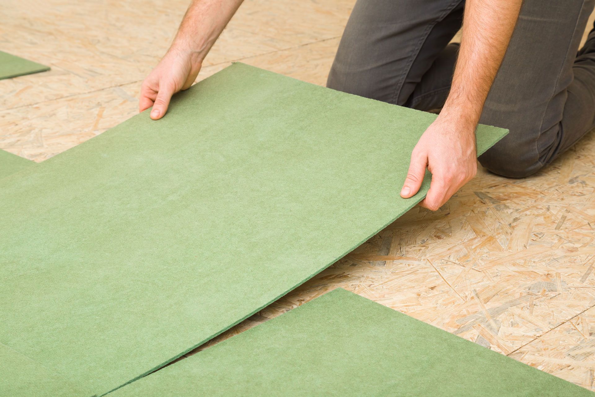Person installing green flooring tiles on a wood subfloor.