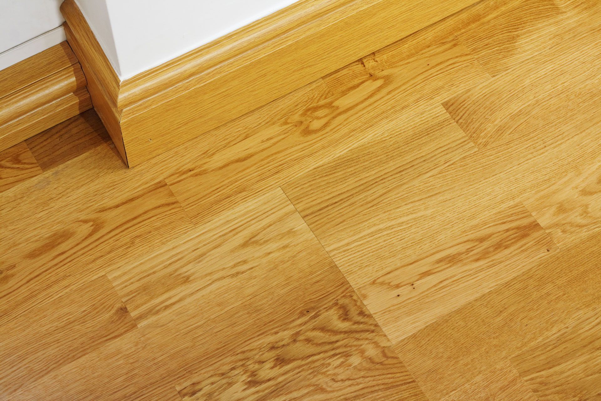 Light oak-colored wood flooring angled against a white wall and baseboard trim.