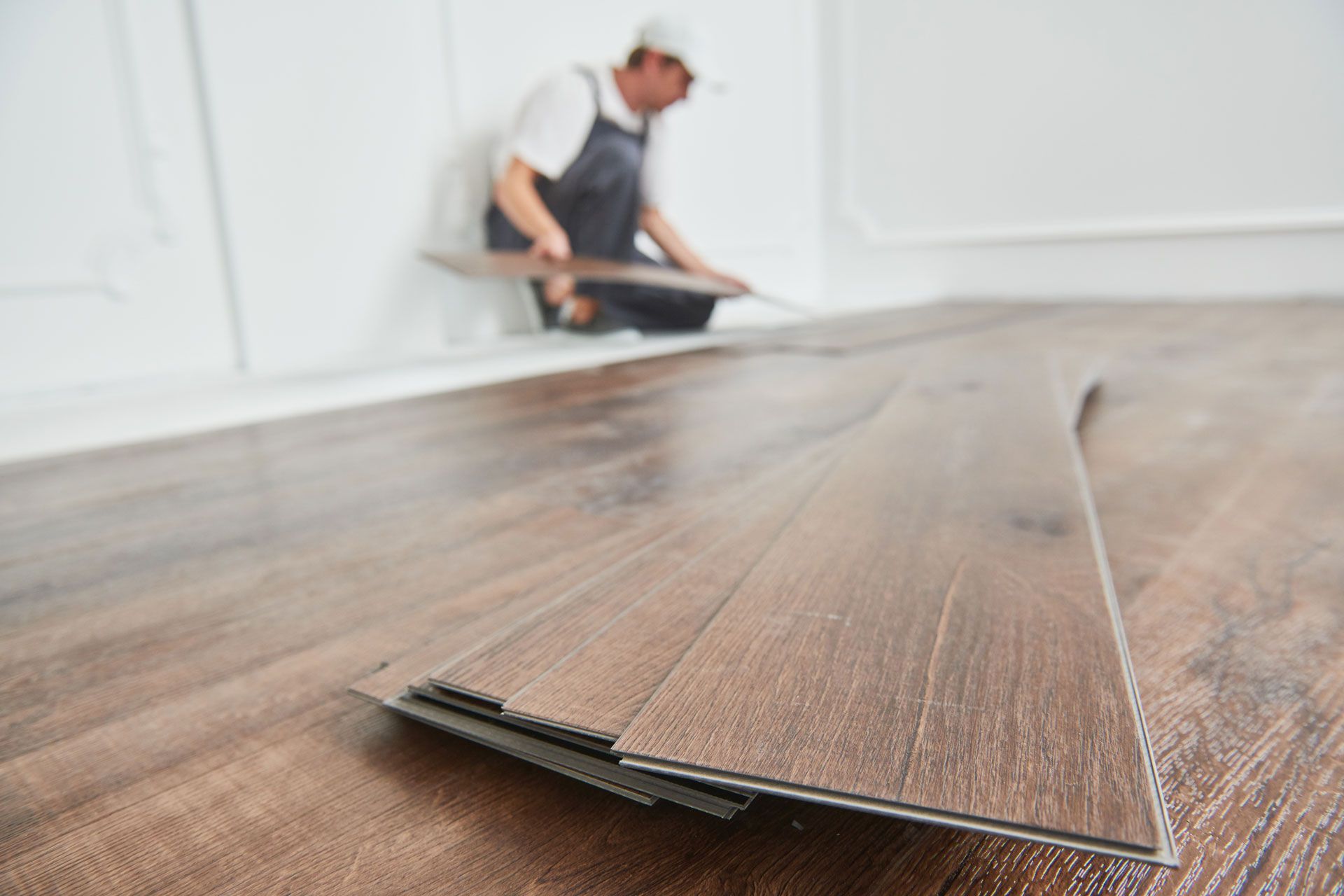 Person installing brown wood-look flooring indoors; floor and stacked planks in focus.