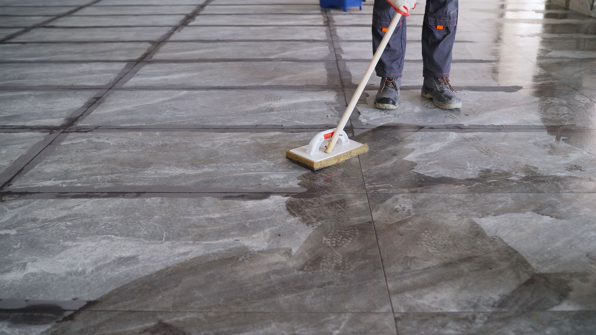 Person mopping a wet concrete floor, using a long-handled squeegee.