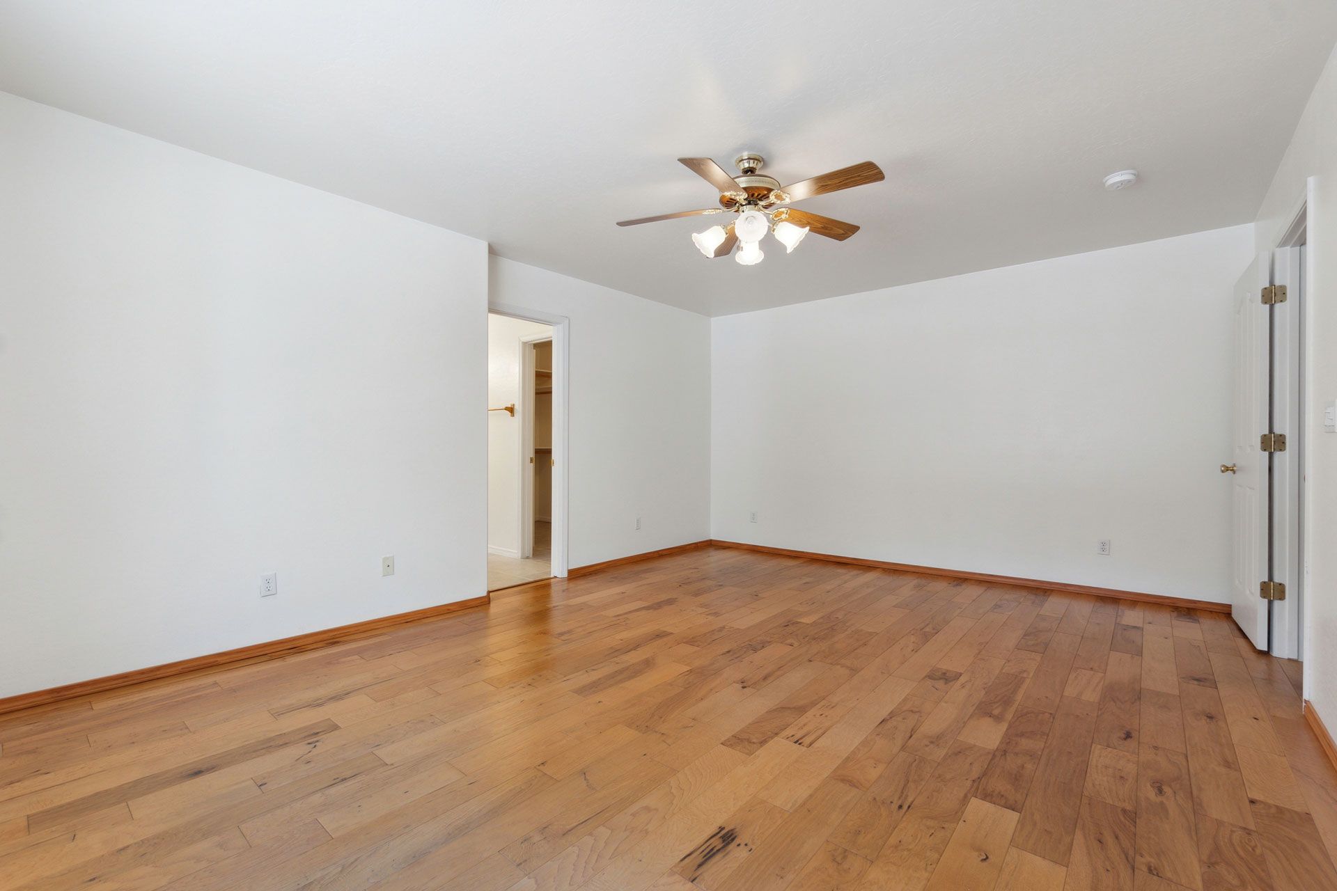 Empty room with hardwood floors, white walls, and a ceiling fan.