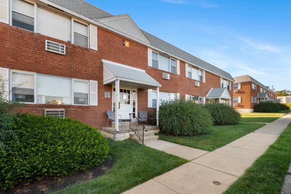 Exterior view of red brick apartment buildings with landscaping and steps leading to entrance.