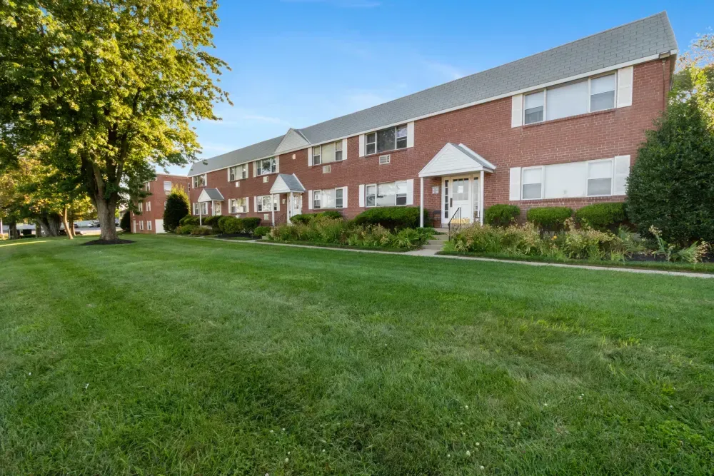 Exterior view of a brick apartment building with green lawn and trees