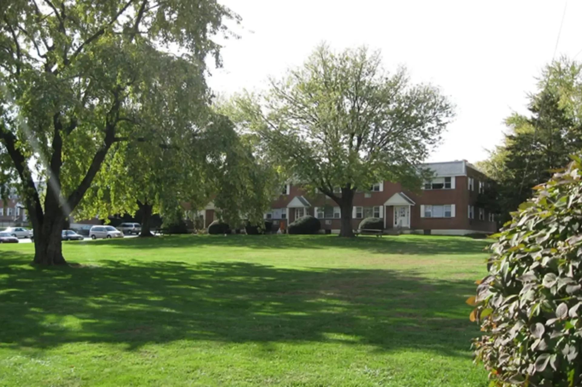 A grassy area with trees and residential building in the background.