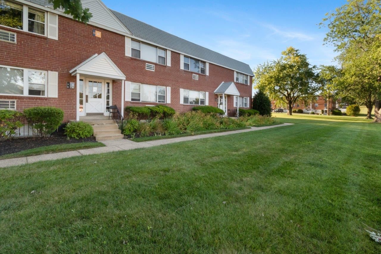 Exterior view of a red brick apartment building with a well-kept lawn and landscaping.