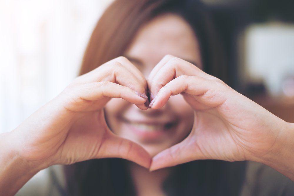 Woman Making Heart Hand Sign Over Her Face — All Body Holistic Health in Hermit Park, QLD